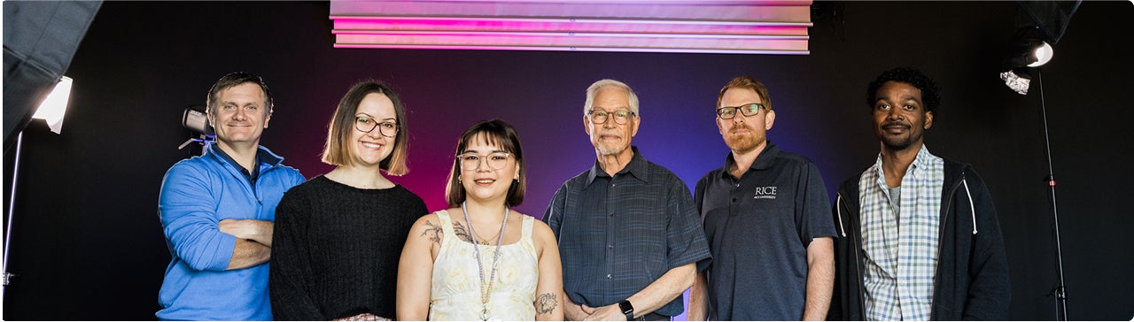A group of people of various ages and backgrounds standing in front of a wall, appearing friendly and relaxed.